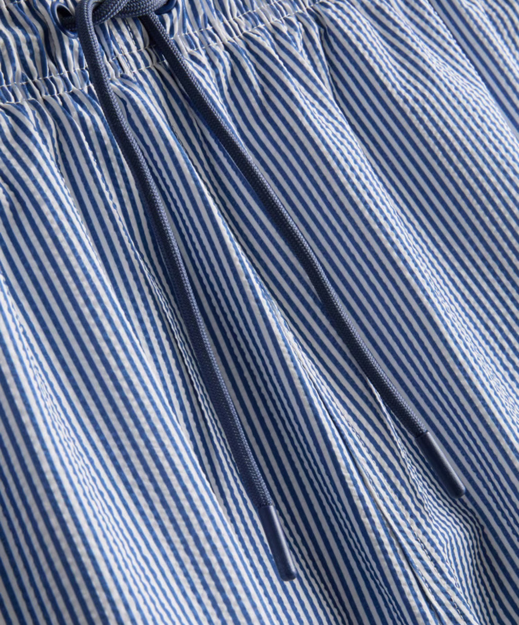 A pair of striped seersucker swimming shorts with a drawstring waistline, pockets, and mesh lining.