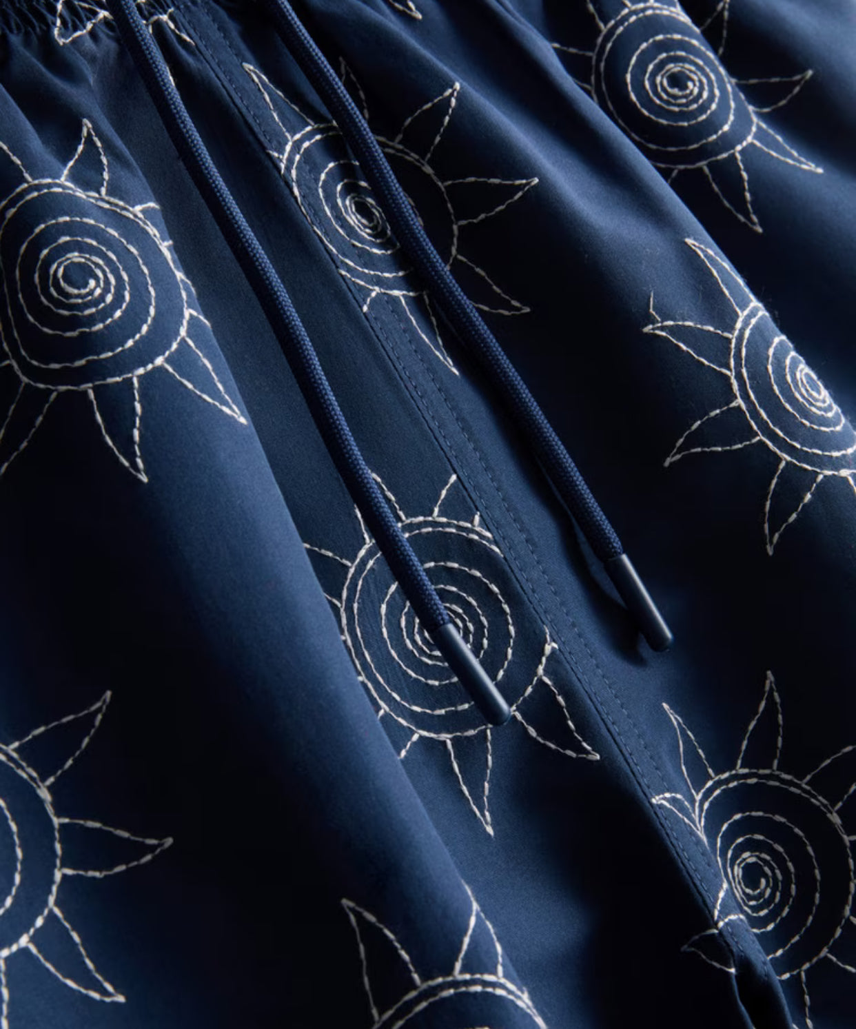 A pair of swimming shorts with embroidered sun design, mesh inner, and drawstring waistline